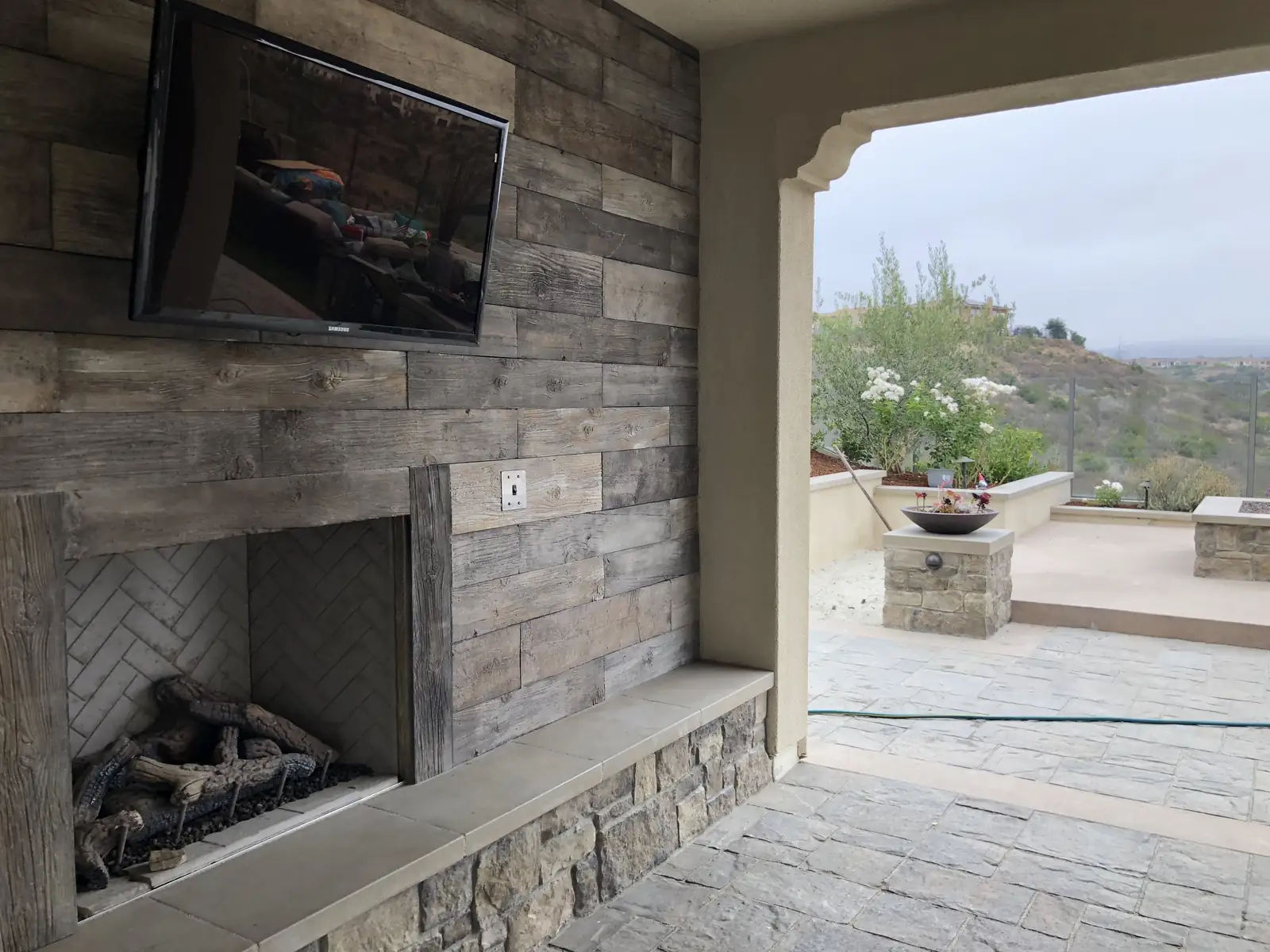 Covered patio with a gas fireplace and outdoor TV by Panjia Outdoors